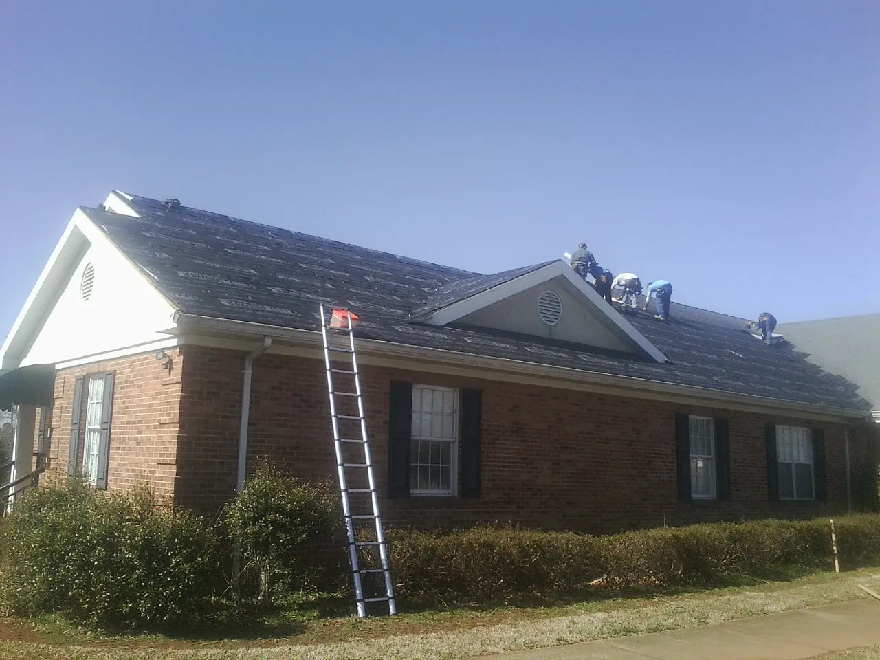 Crew tearing shingles off a brick ranch roof with a ladder set — Emergency Roof Repair work by our crew in Orange Park