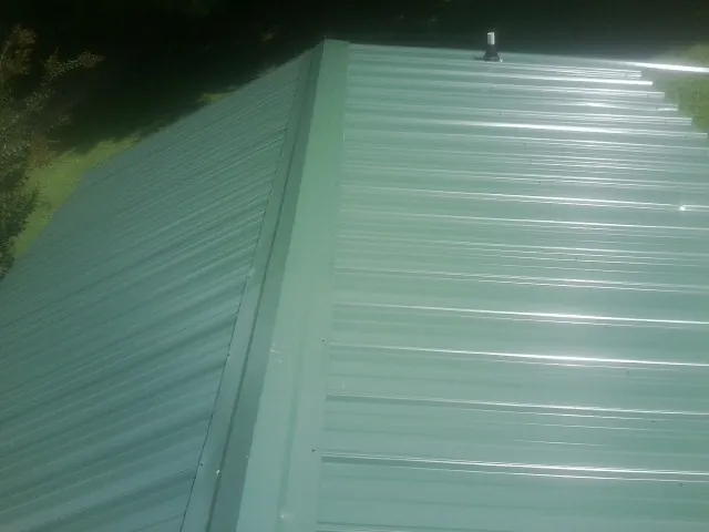 New green metal panels meeting at the ridge of a roof — Flat Roof Repair work by our crew in Orange Park