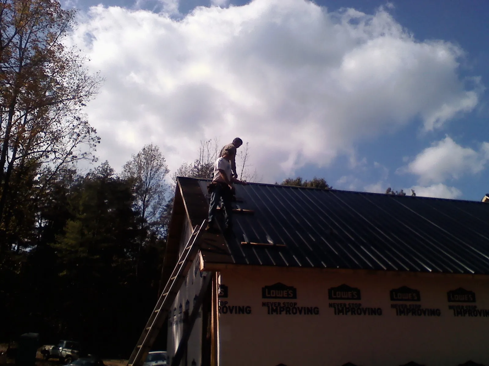 Roofer fastening dark metal panels high against a cloudy sky, from a Roof Inspection job in Orange Park