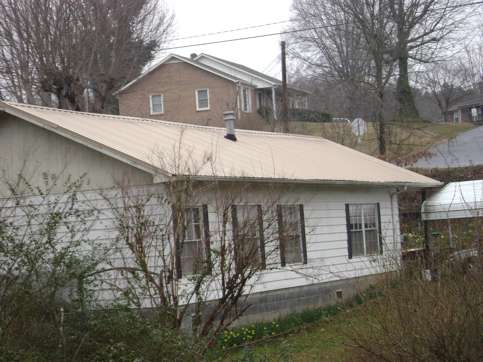 Tan metal roof on a white sided house set into a hillside — Commercial Roofing by Roofing Brothers in Orange Park