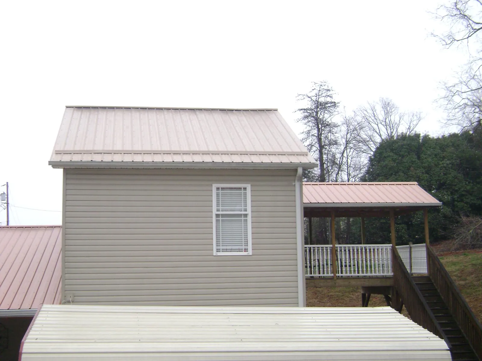 Tan metal roofs on a two story addition and attached porch, from a Roof Replacement job in Orange Park